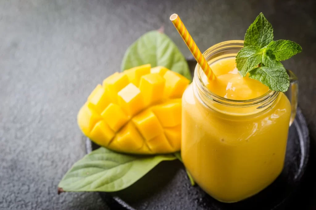 Tasty mango smoothie in a glass jar with mango slices a side.
