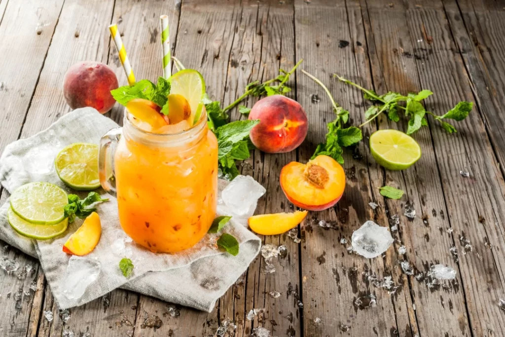 The Peach Probiotic Smoothie is in a big glass jar with peach a side on a wooden table.