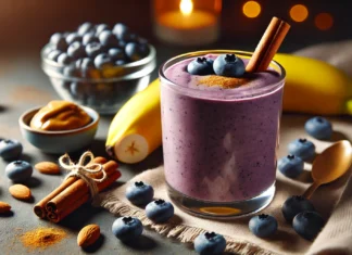 A creamy blueberry-banana relaxation smoothie in a clear glass, surrounded by fresh blueberries, a ripe banana, cinnamon sticks, and almond butter. The smoothie has a rich purple-blue hue with a smooth texture, set against a softly lit, cozy background for a relaxing nighttime ambiance.