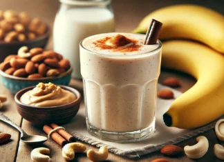 A creamy cashew-banana smoothie in a glass, placed on a wooden table with a ripe banana, cashew butter, cinnamon sticks, and a glass of almond milk. The smoothie has a velvety texture with a sprinkle of cinnamon, creating a cozy and relaxing sleep-supporting drink.