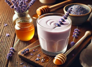A soothing, floral-infused smoothie in a glass, featuring honey, lavender, and coconut milk. The smoothie has a creamy, pale lavender hue and is placed on a wooden table with a small bowl of dried lavender, a drizzle of honey, and a spoon resting nearby. The setting is warm and tranquil, evoking a sense of relaxation.