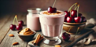 A creamy tart cherry smoothie in a clear glass, garnished with a sprinkle of cinnamon and almonds, placed on a rustic wooden surface. Fresh tart cherries and a small bowl of almond butter sit beside the glass, creating a cozy nighttime ambiance.