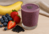 A vibrant berry smoothie blended with black beans, banana, strawberries, blueberries, and chia seeds, displayed in a glass with fresh fruits and black beans on the side.