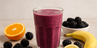 A rich purple smoothie made with blackberries, orange, lemon, banana, and flaxseed, surrounded by fresh fruit and seeds on a bright, rustic surface to highlight cardiovascular-supportive ingredients.