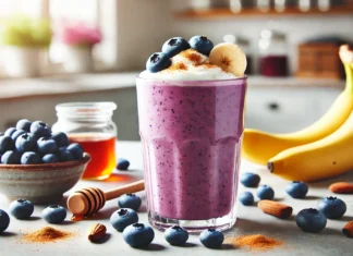 A creamy blueberry-banana smoothie in a tall glass, topped with fresh blueberries and a sprinkle of cinnamon, set in a bright kitchen with natural lighting.