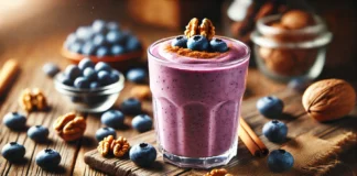 A creamy blueberry smoothie in a clear glass, garnished with walnuts and a sprinkle of cinnamon. The smoothie has a rich purple hue and is placed on a wooden table with fresh blueberries and walnut pieces scattered around, creating a cozy and inviting scene.