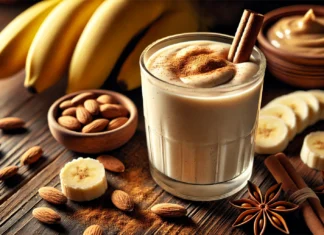 A thick and creamy banana smoothie garnished with cinnamon, surrounded by fresh bananas, almonds, almond butter, and anise spice on a wooden surface, creating a warm and cozy nighttime atmosphere.