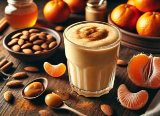 A thick and creamy clementine smoothie garnished with cinnamon, surrounded by fresh clementines, almonds, almond butter, and honey on a wooden surface, creating a warm and cozy nighttime atmosphere.
