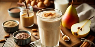 A creamy and energizing Creamy Pear & Almond Fuel Smoothie in a tall glass with a smooth beige color. Garnished with a sprinkle of cinnamon, the smoothie sits on a wooden surface alongside a ripe pear, a small dish of almond butter, flaxseeds, and a glass of almond milk, highlighting its protein-rich and energy-sustaining ingredients.