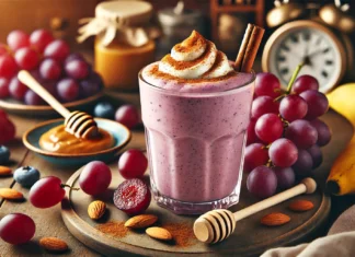 A creamy, purple-red smoothie in a clear glass, made with red grapes, almond milk, banana, and almond butter. The smoothie is garnished with a sprinkle of cinnamon and a drizzle of honey, surrounded by fresh ingredients in a warm, cozy setting.