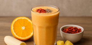 A vibrant heart-healthy smoothie made with goji berries, orange, banana, pineapple, coconut water, and chia seeds, presented with fresh fruit ingredients on a wooden surface.