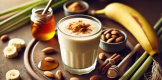 A thick and creamy banana smoothie garnished with cinnamon and honey, placed on a wooden surface with almonds, almond butter, and fresh lemongrass, creating a warm and relaxing atmosphere.