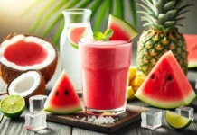 A bright pinkish-red Watermelon Coconut Hydration Smoothie in a clear glass, surrounded by fresh watermelon cubes, coconut water, pineapple chunks, lime halves, honey, and ice cubes on a wooden surface with soft, natural lighting.